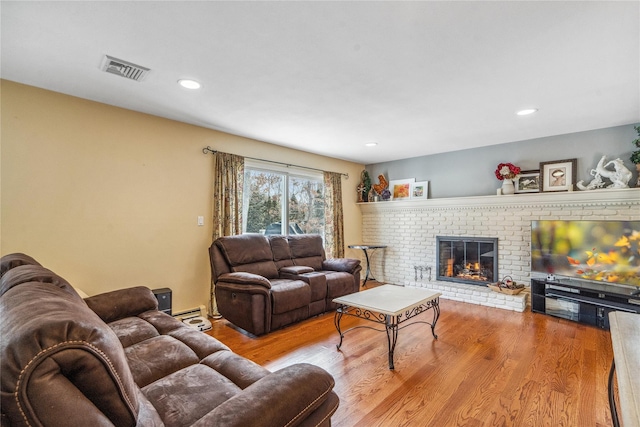 living area with light wood-style flooring, a brick fireplace, visible vents, and recessed lighting