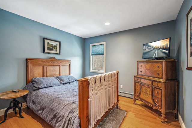 bedroom with a baseboard heating unit, light wood-style flooring, and baseboards