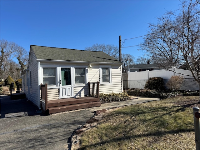 bungalow featuring a shingled roof, fence, and a front lawn