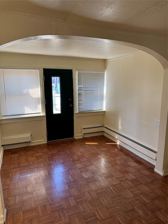 foyer entrance with arched walkways, a textured ceiling, and a baseboard radiator