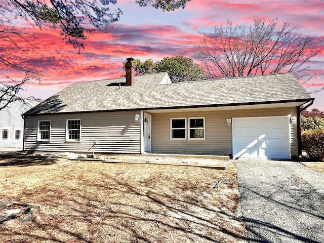 view of front facade with driveway, a shingled roof, a chimney, and an attached garage