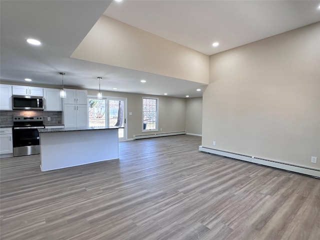 kitchen with white cabinets, appliances with stainless steel finishes, open floor plan, hanging light fixtures, and baseboard heating