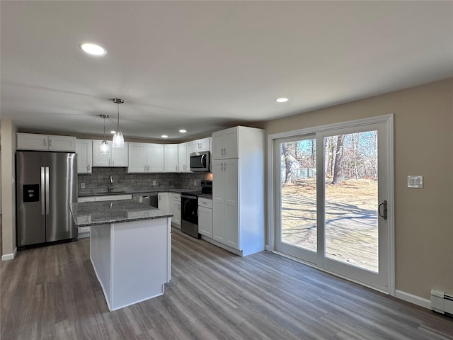 kitchen with dark stone countertops, decorative light fixtures, stainless steel appliances, white cabinetry, and a sink