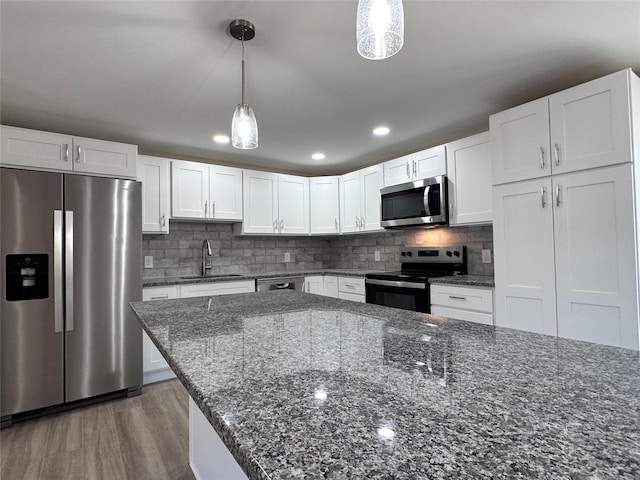 kitchen featuring pendant lighting, backsplash, appliances with stainless steel finishes, white cabinetry, and a sink