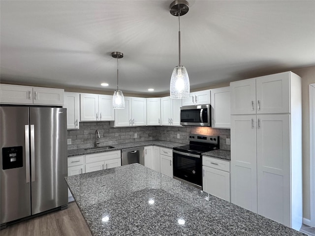 kitchen with a sink, white cabinetry, hanging light fixtures, appliances with stainless steel finishes, and dark stone countertops