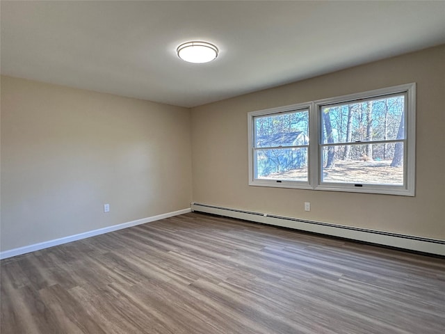 empty room with a baseboard heating unit, wood finished floors, and baseboards