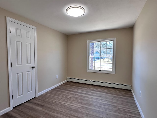 unfurnished room featuring baseboards, baseboard heating, and wood finished floors