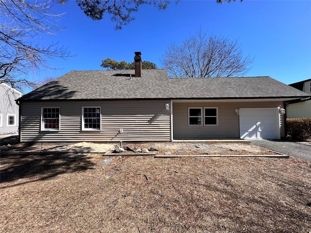 rear view of property featuring a chimney, aphalt driveway, roof with shingles, and an attached garage