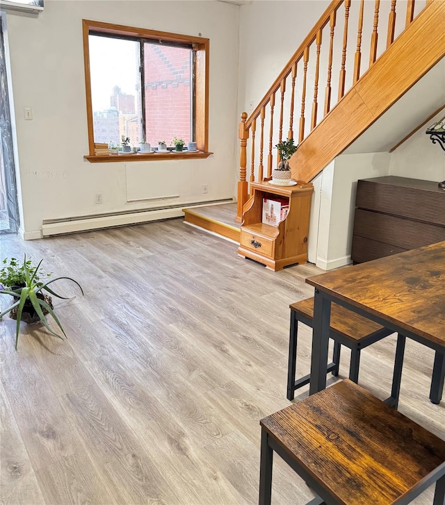 living room featuring light wood-type flooring, baseboard heating, and stairs