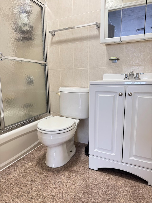 bathroom featuring toilet, shower / bath combination with glass door, vanity, tile walls, and decorative backsplash