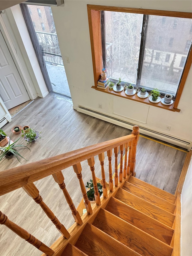 stairs with a baseboard heating unit and wood finished floors