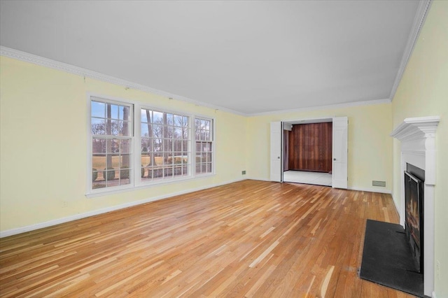 unfurnished living room with light wood-style flooring, a fireplace with flush hearth, visible vents, baseboards, and crown molding