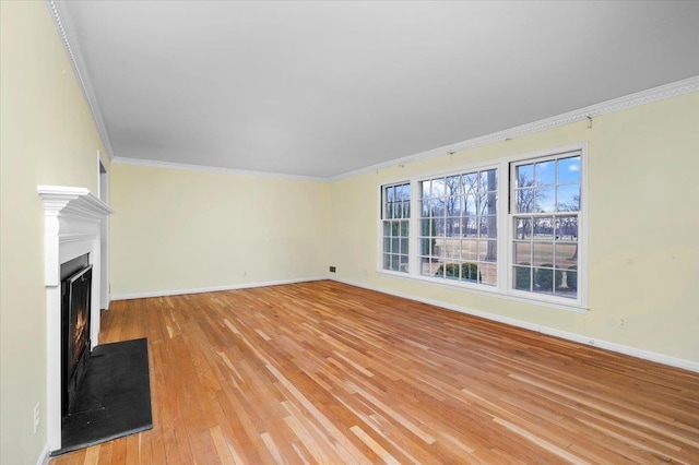 unfurnished living room with baseboards, crown molding, a lit fireplace, and light wood finished floors