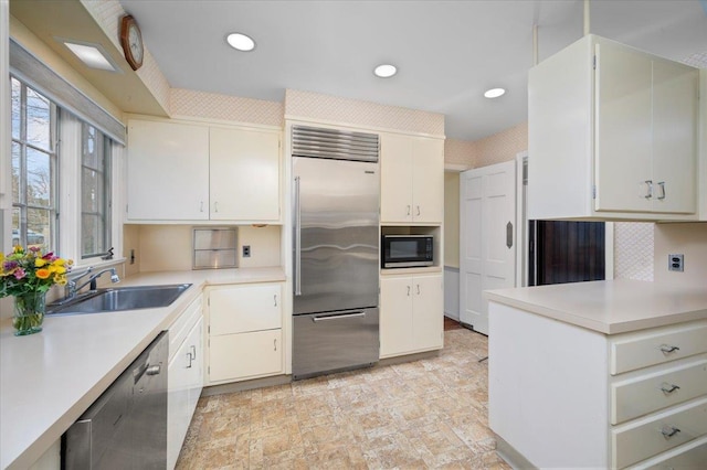 kitchen with tasteful backsplash, light countertops, white cabinets, a sink, and built in appliances