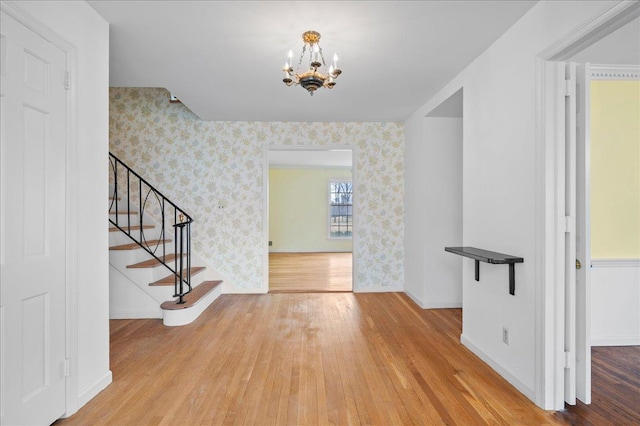 entryway featuring stairs, wood finished floors, a chandelier, and wallpapered walls