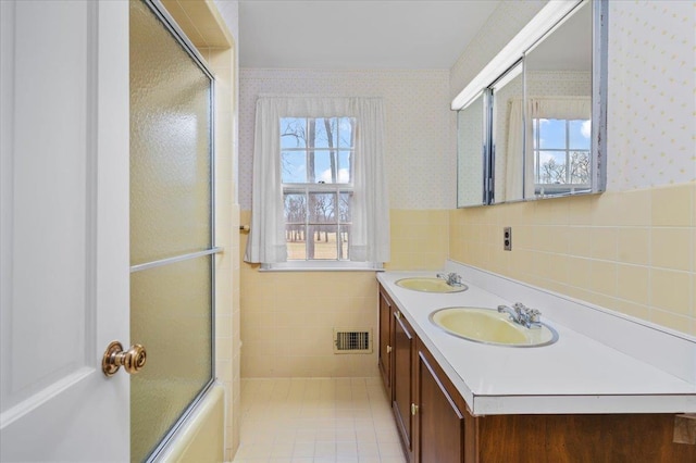 bathroom featuring a wainscoted wall, visible vents, a sink, and wallpapered walls