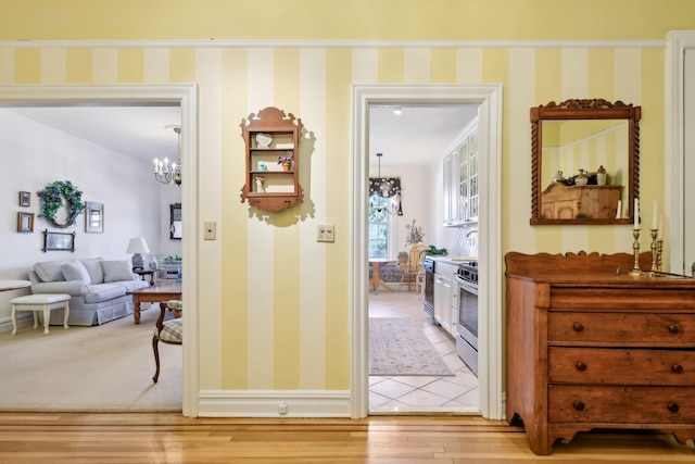 corridor with wallpapered walls, light wood-style flooring, baseboards, and an inviting chandelier