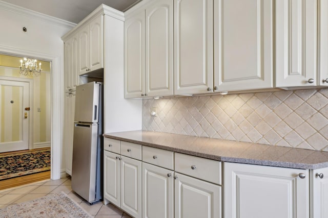 kitchen with light tile patterned floors, white cabinets, light countertops, freestanding refrigerator, and crown molding