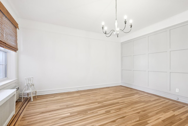 unfurnished dining area with light wood finished floors, radiator heating unit, an inviting chandelier, crown molding, and a decorative wall