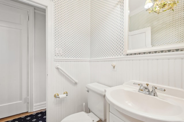 bathroom featuring toilet, a wainscoted wall, crown molding, and wallpapered walls