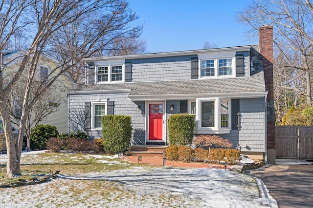 view of front of property featuring driveway, roof with shingles, a chimney, and fence