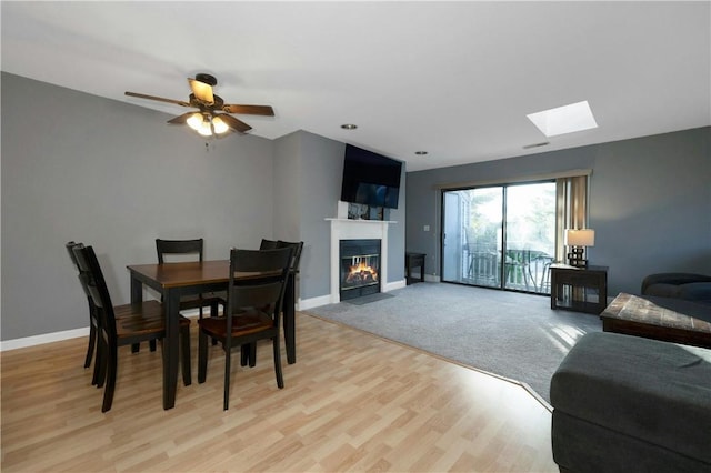 dining area with light wood-style floors, a fireplace with flush hearth, baseboards, and a ceiling fan