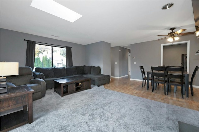 carpeted living area with a skylight, visible vents, ceiling fan, wood finished floors, and baseboards