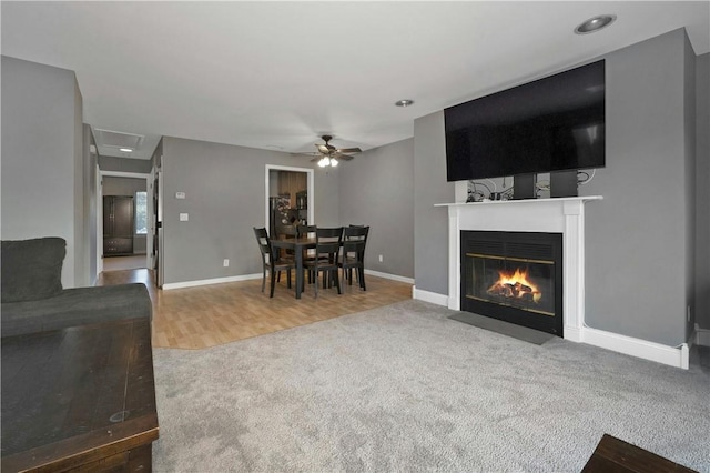 living area with a fireplace with flush hearth, carpet flooring, ceiling fan, wood finished floors, and baseboards