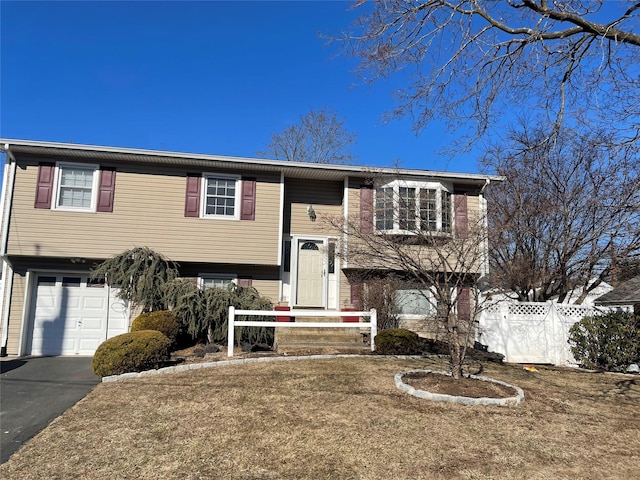 bi-level home with a garage, fence, and aphalt driveway