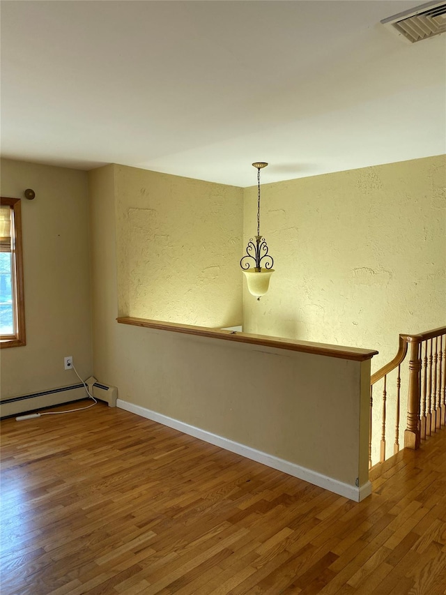 empty room featuring a baseboard radiator, baseboards, visible vents, and wood finished floors