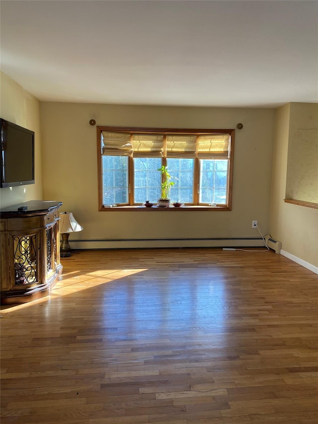 unfurnished living room with a baseboard heating unit, baseboards, and wood finished floors