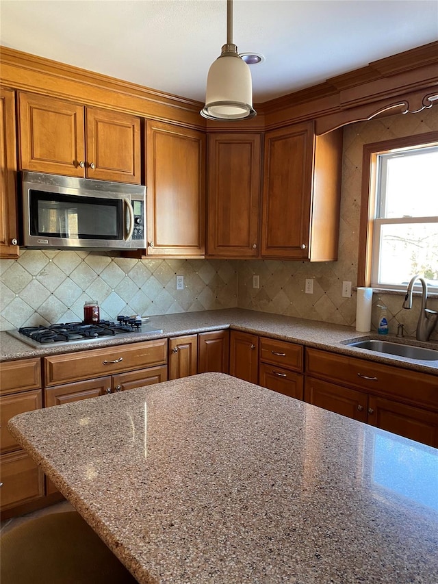 kitchen featuring brown cabinetry, stainless steel microwave, a sink, gas stovetop, and backsplash