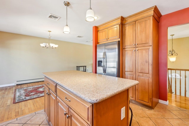 kitchen with stainless steel refrigerator with ice dispenser, visible vents, a baseboard heating unit, a kitchen island, and light stone countertops