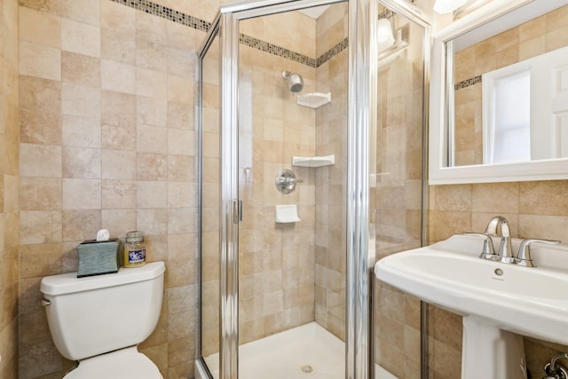 bathroom with toilet, a stall shower, tile walls, and a sink