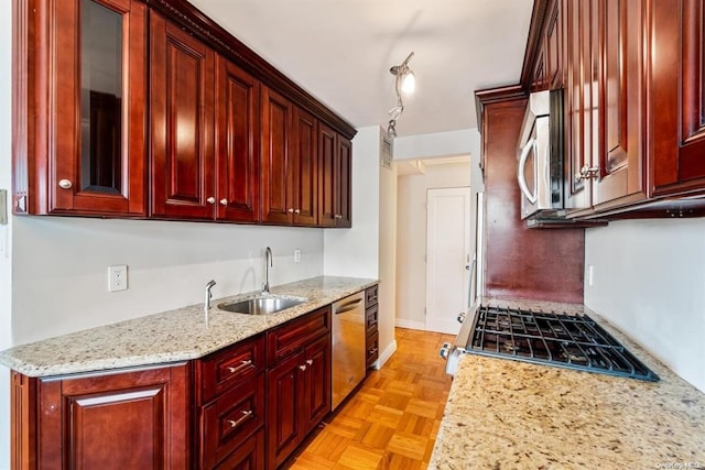 kitchen featuring stainless steel appliances, reddish brown cabinets, a sink, and light stone countertops