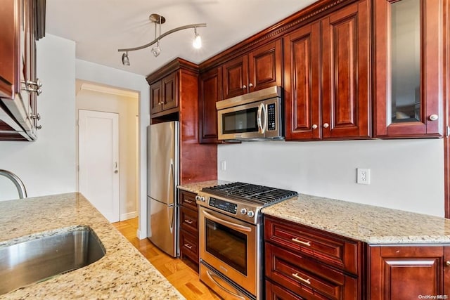 kitchen featuring stainless steel appliances, dark brown cabinets, a sink, and light stone countertops