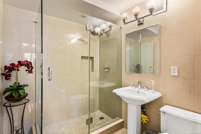 full bath with a stall shower, a sink, tile walls, and toilet