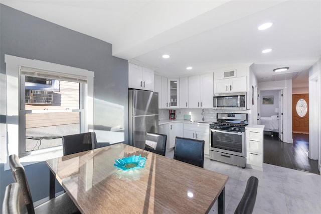 kitchen with a sink, white cabinets, appliances with stainless steel finishes, decorative backsplash, and glass insert cabinets