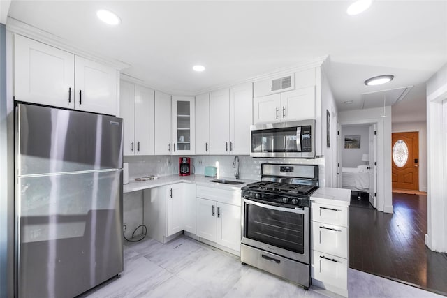 kitchen with stainless steel appliances, a sink, white cabinets, light countertops, and glass insert cabinets