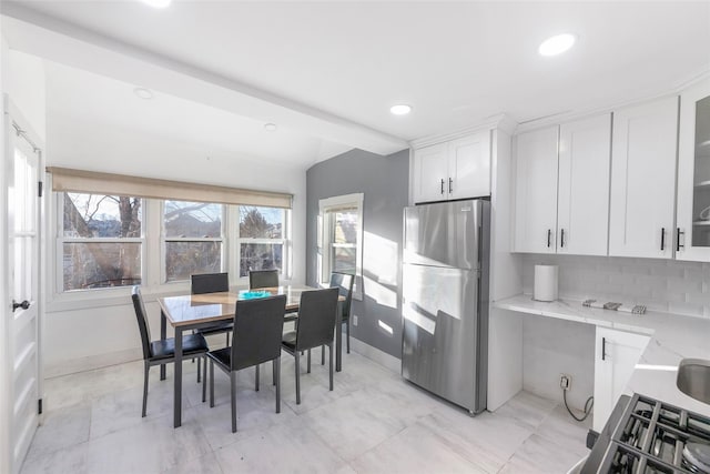 kitchen with tasteful backsplash, white cabinets, glass insert cabinets, freestanding refrigerator, and light stone countertops