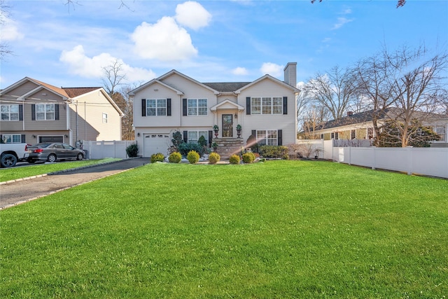 split foyer home with a garage, fence, driveway, a chimney, and a front yard