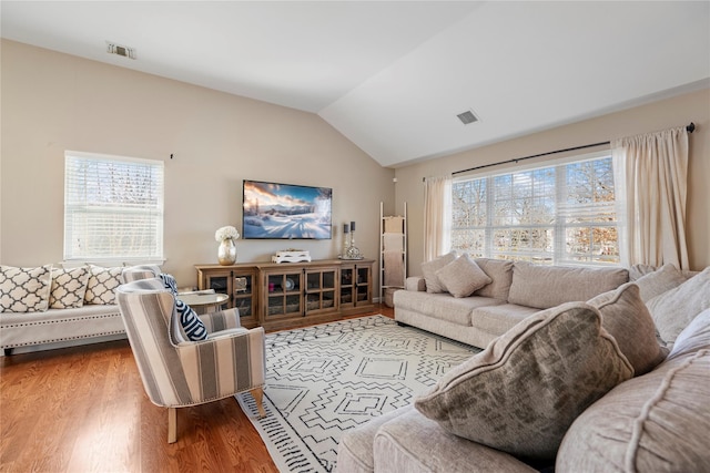 living room with lofted ceiling, wood finished floors, visible vents, and a healthy amount of sunlight