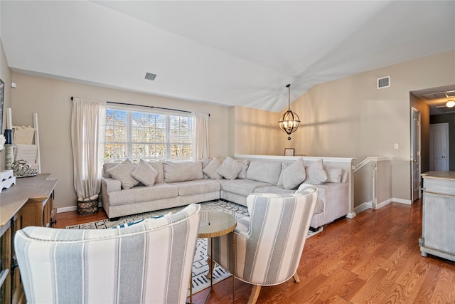 living room with visible vents, vaulted ceiling, a notable chandelier, and wood finished floors