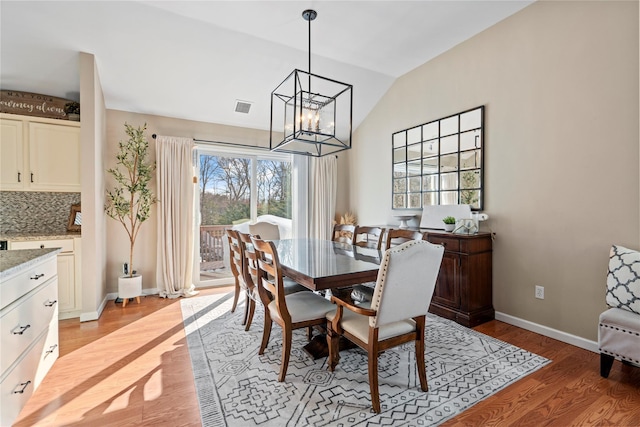 dining space featuring baseboards, visible vents, lofted ceiling, an inviting chandelier, and light wood-style floors