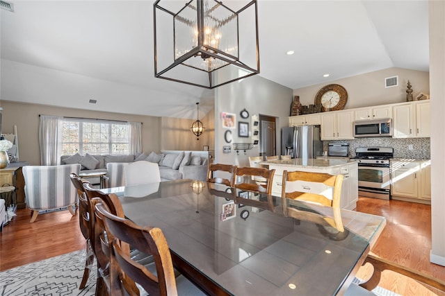 dining room with a chandelier, lofted ceiling, light wood-type flooring, and visible vents