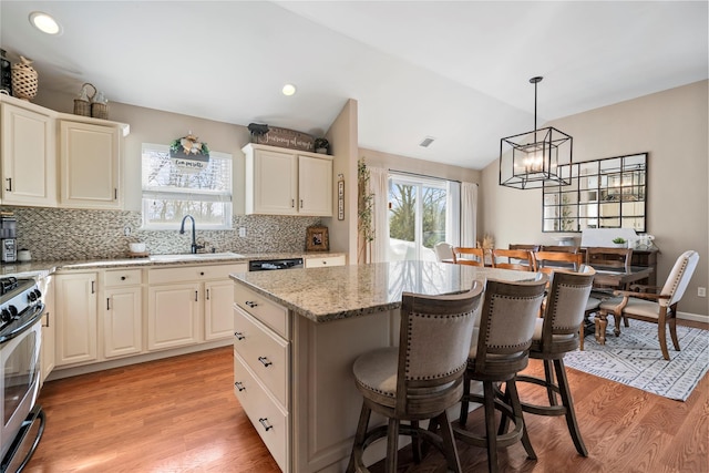 kitchen with stainless steel range, lofted ceiling, a center island, a kitchen bar, and a sink