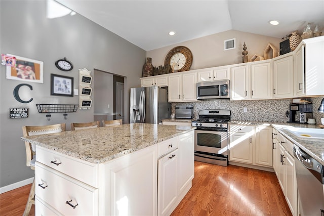 kitchen featuring a center island, stainless steel appliances, lofted ceiling, tasteful backsplash, and visible vents