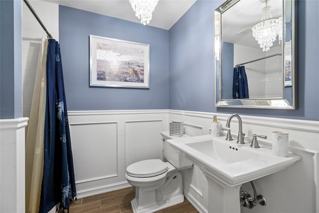 bathroom with wood finished floors, wainscoting, toilet, and an inviting chandelier