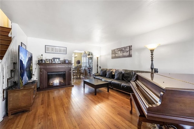 living room with stairs, arched walkways, wood finished floors, and a glass covered fireplace