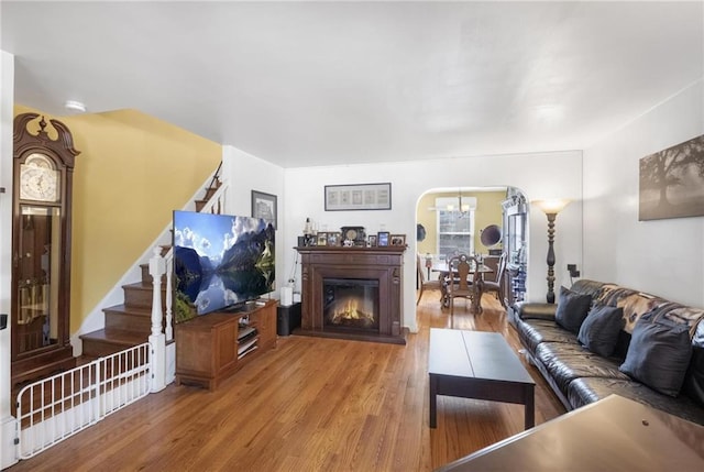 living room with arched walkways, a glass covered fireplace, stairway, and wood finished floors